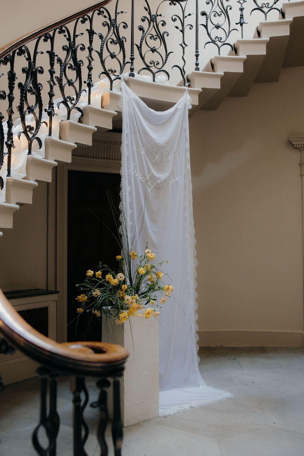 White wedding veil draped over staircase railing beside yellow floral arrangement in elegant venue with ornate ironwork.