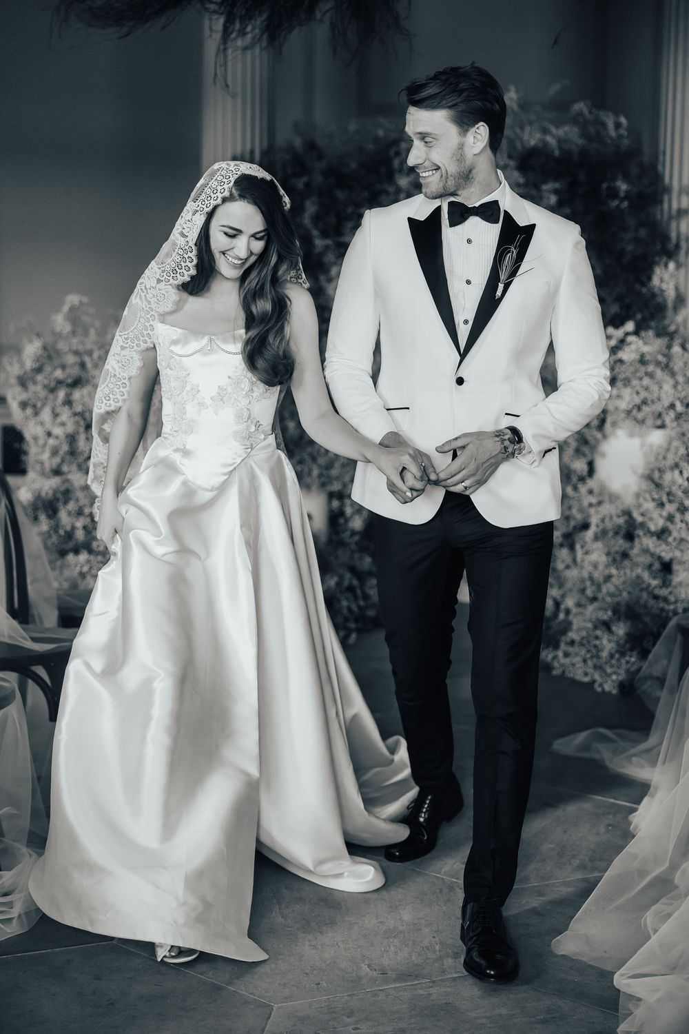 Black and white photo of a smiling bride and groom walking together at their elegant wedding ceremony.