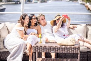 Four women in white outfits taking a selfie on a yacht deck on a sunny day.