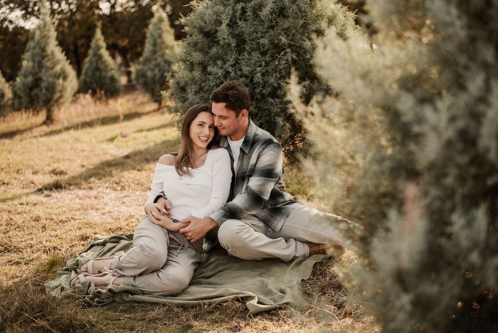 Couple sitting together on a blanket at a Christmas tree farm, sharing a tender moment outdoors.