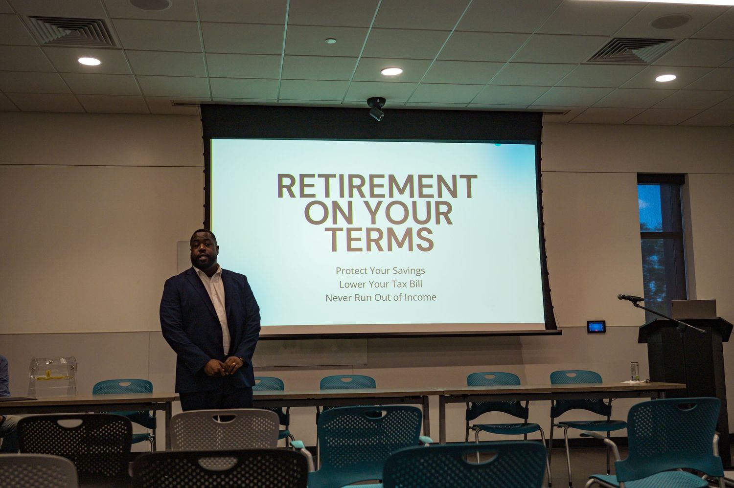 Financial speaker stands before Retirement On Your Terms projected screen in a seminar.