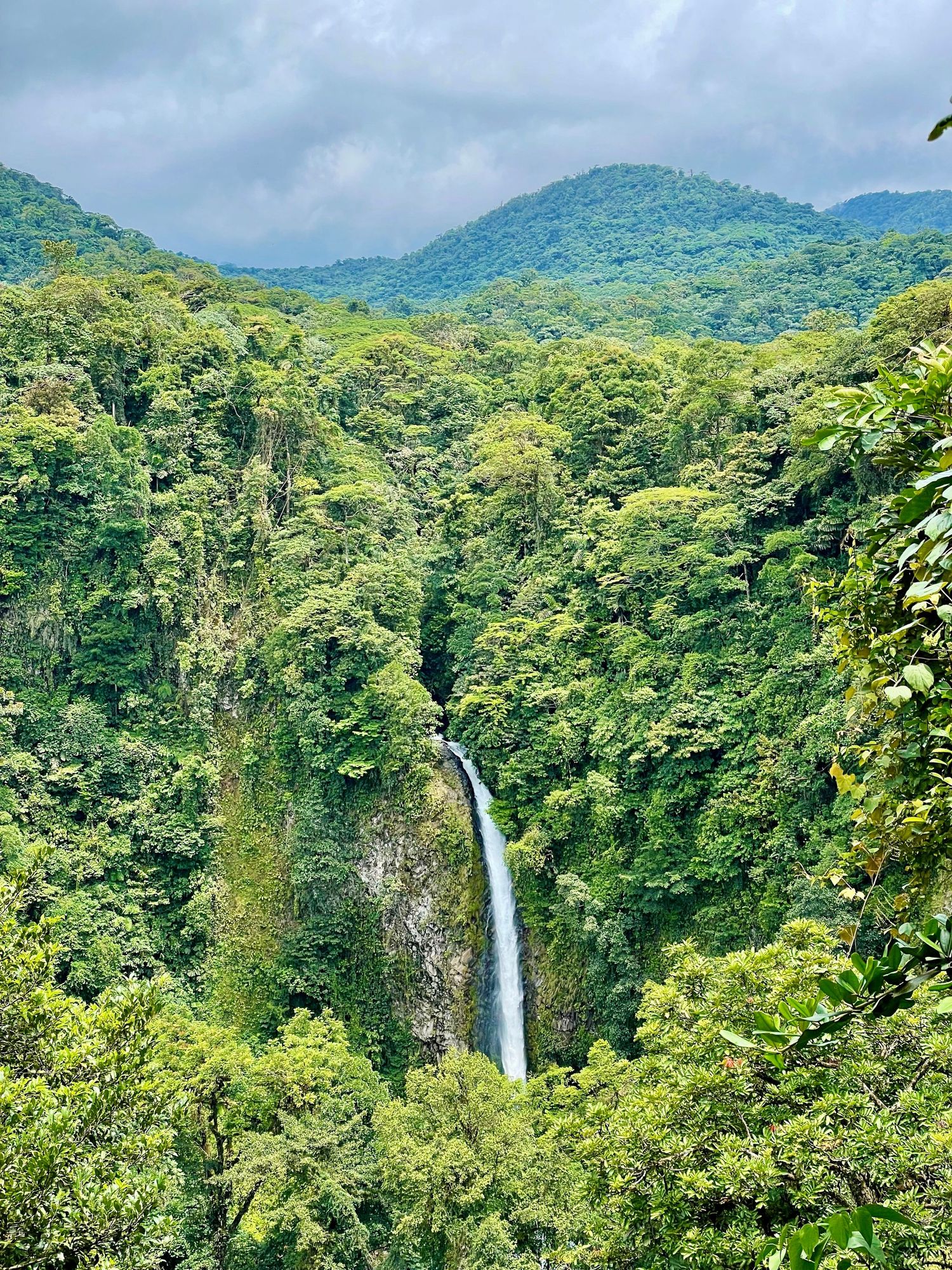 Tall waterfall cascading through lush green tropical rainforest of Costa Rica with misty mountains in background