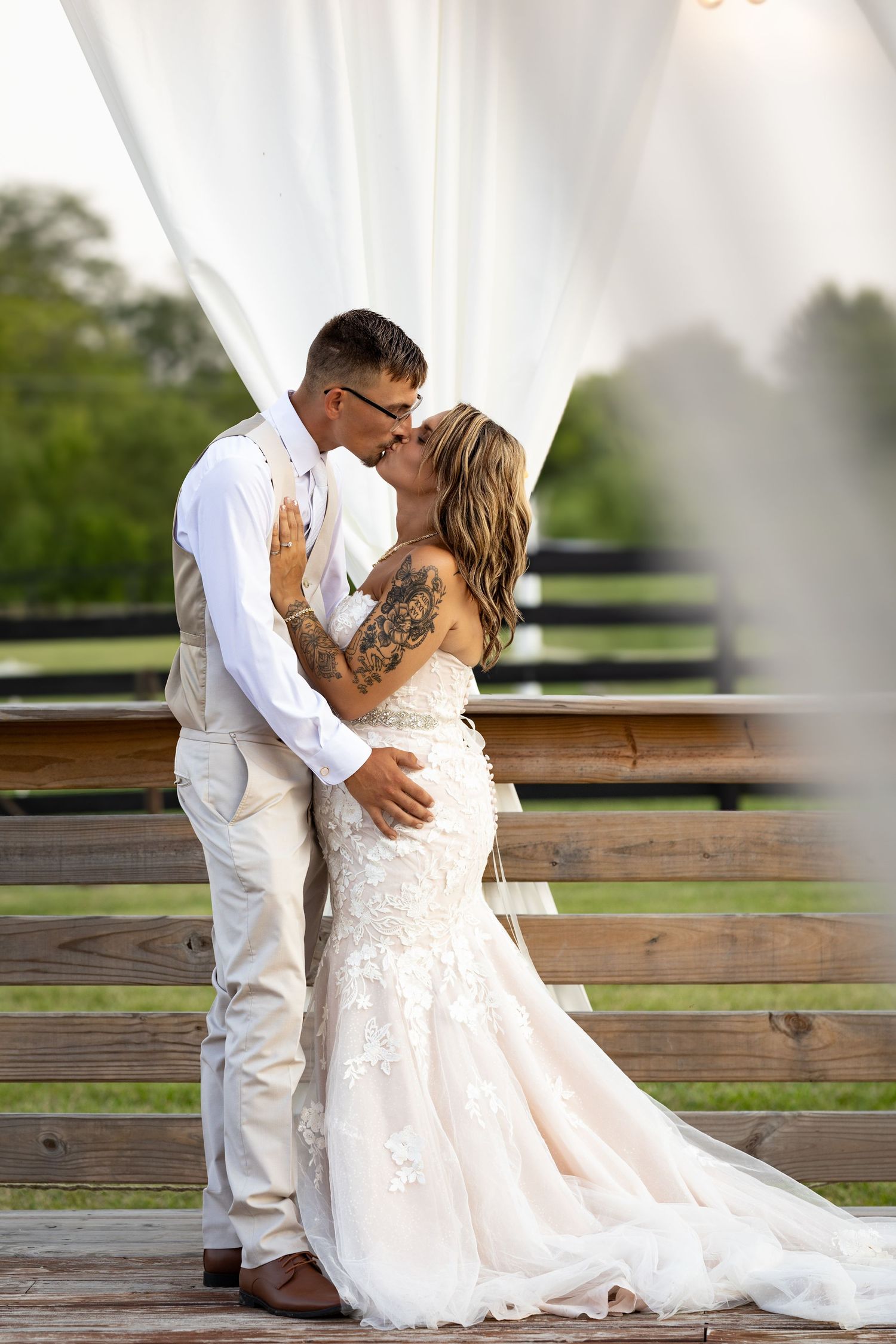 Bride and groom sharing a romantic first kiss under white draped fabric at an outdoor wedding.