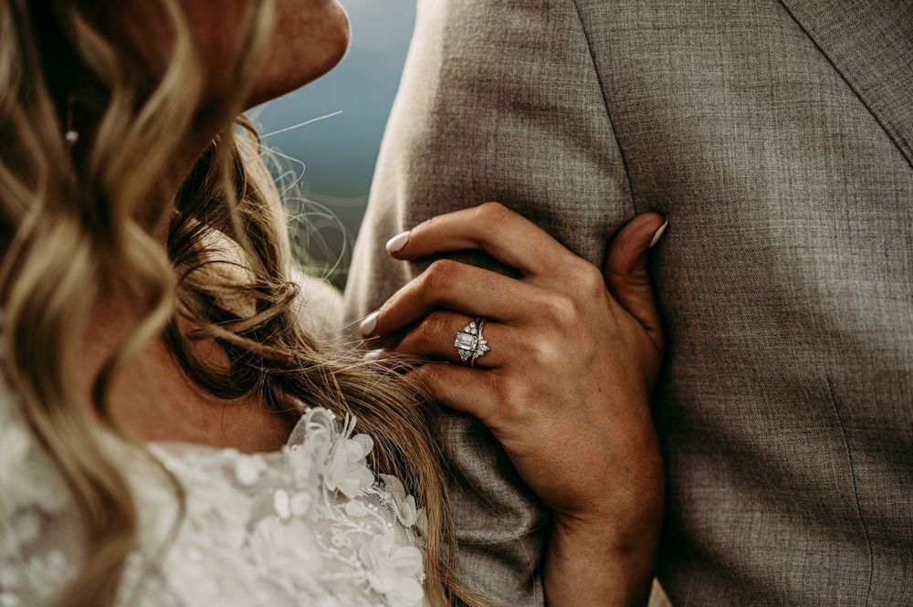 Bride resting head on groom's chest, showcasing a stunning diamond engagement ring on her hand.