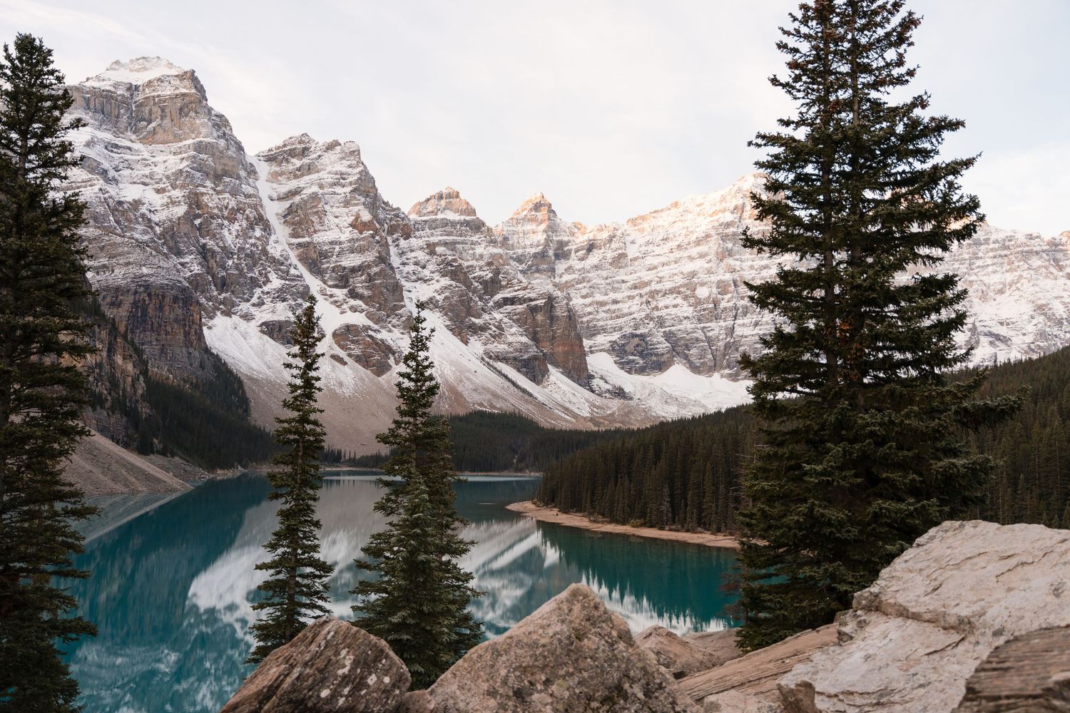 Snow-capped mountains reflect in turquoise Moraine Lake surrounded by evergreen trees in Banff National Park, Canada.