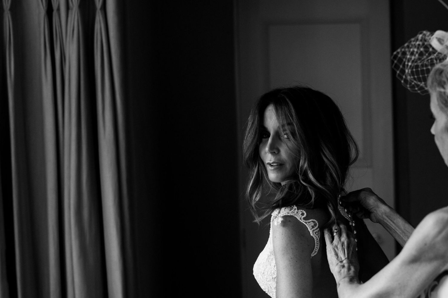 Groom emotional seeing bride in white wedding dress and veil for first time, woman in black dress behind him.