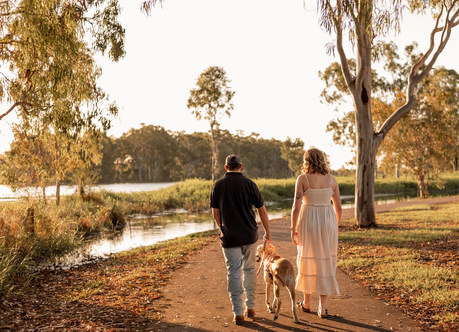 Couple sharing a romantic kiss at golden hour near a tranquil lake surrounded by trees.