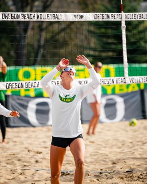 Oregon Beach Volleyball player in white long sleeve shirt celebrates on sandy court near the net during a sunny match.