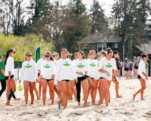 University of Oregon female beach volleyball players in white jerseys walking on sand during a sunny outdoor match.