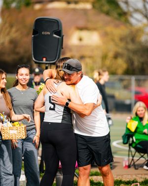 Athlete in jersey number 5 receives a warm hug from a man in white shirt at an outdoor sports event.