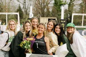 University of Oregon athlete in jersey poses with smiling friends holding flowers at outdoor sports event.