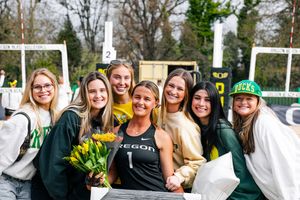 University of Oregon athlete in jersey holds yellow tulips surrounded by smiling friends at an outdoor track event.
