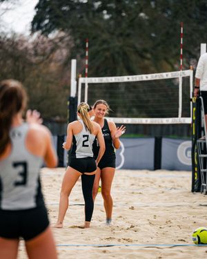 Two beach volleyball players in black and white uniforms celebrate on a sand court near the net during a match.