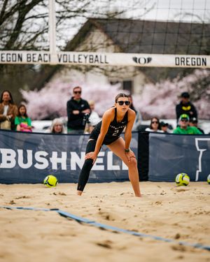 Female beach volleyball player in black outfit digs a ball on sand court at Oregon Beach Volleyball tournament.