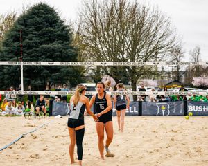 Two beach volleyball players in black and white uniforms celebrate on a sandy court during an Oregon Beach Volleyball match.