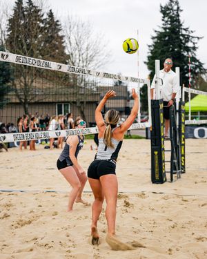 Two female beach volleyball players set the ball over the net during an outdoor sand court match.