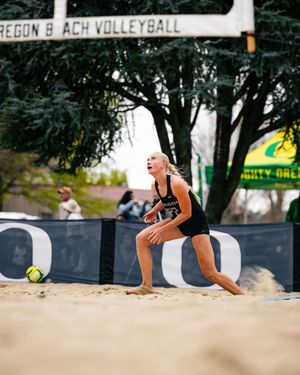 Female beach volleyball player in black uniform digs for the ball on sand court at Oregon Beach Volleyball.
