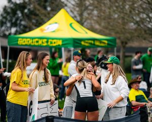 Oregon Ducks fans celebrate together near a GoDucks.com tent at an outdoor sports event.