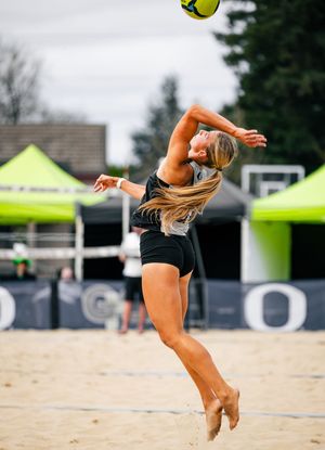 Female beach volleyball player leaping to spike a ball on a sandy court during a competitive outdoor match.