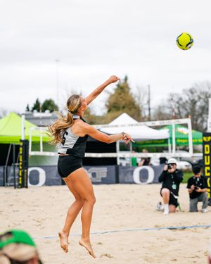 Female beach volleyball player jumping to spike a yellow ball during an outdoor match on a sand court.