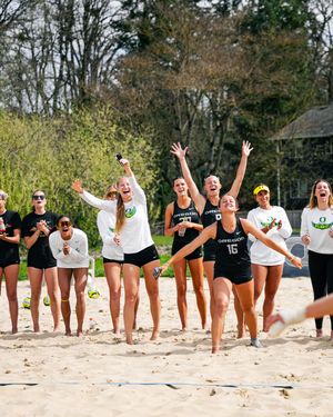 University of Oregon womens beach volleyball team celebrating on a sandy court outdoors during a sunny spring match.