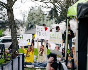 Fans hold signs cheering at outdoor beach volleyball match, including We Love Toosh sign.