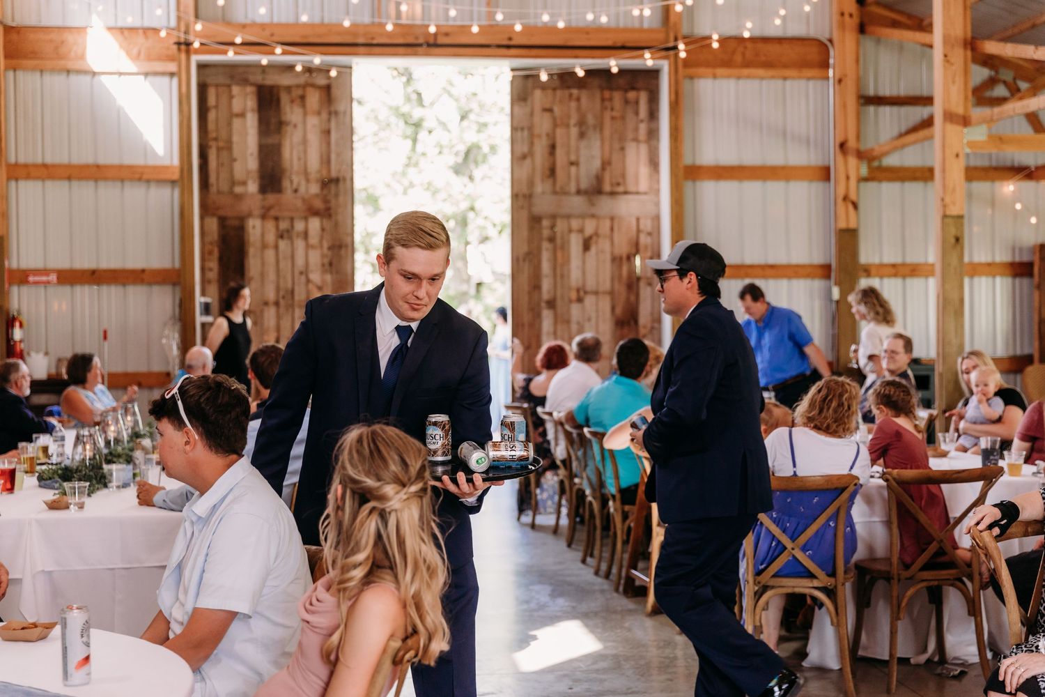 Bridesmaids dancing joyfully at a rustic barn wedding reception with guests seated at decorated tables.