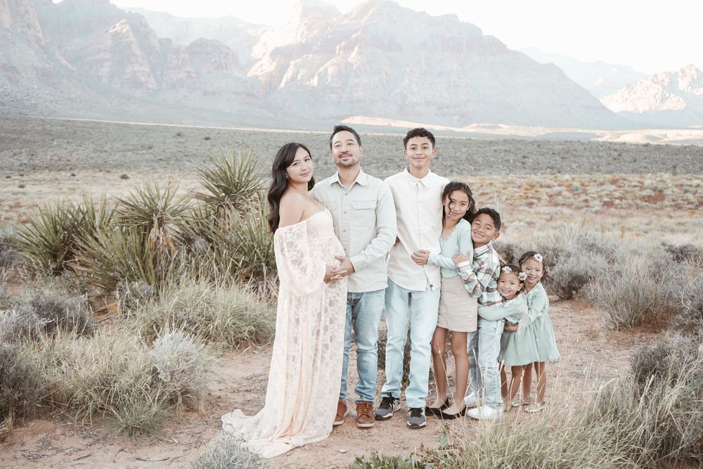 Family maternity photo shoot in desert landscape with red rock mountains, parents and three children posing together outdoors.
