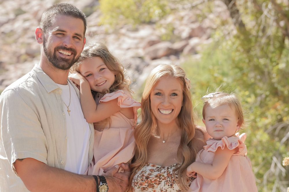 Happy family of four smiling together outdoors in a warm desert landscape setting.