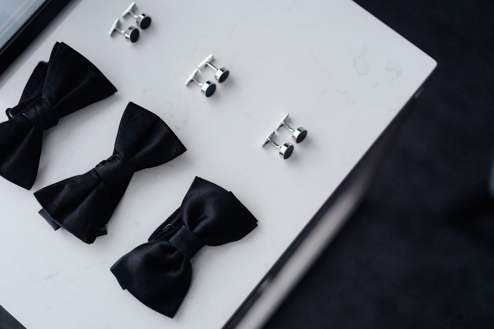 Three black bow ties and silver cufflinks displayed on a white surface for a formal wedding or black tie event.