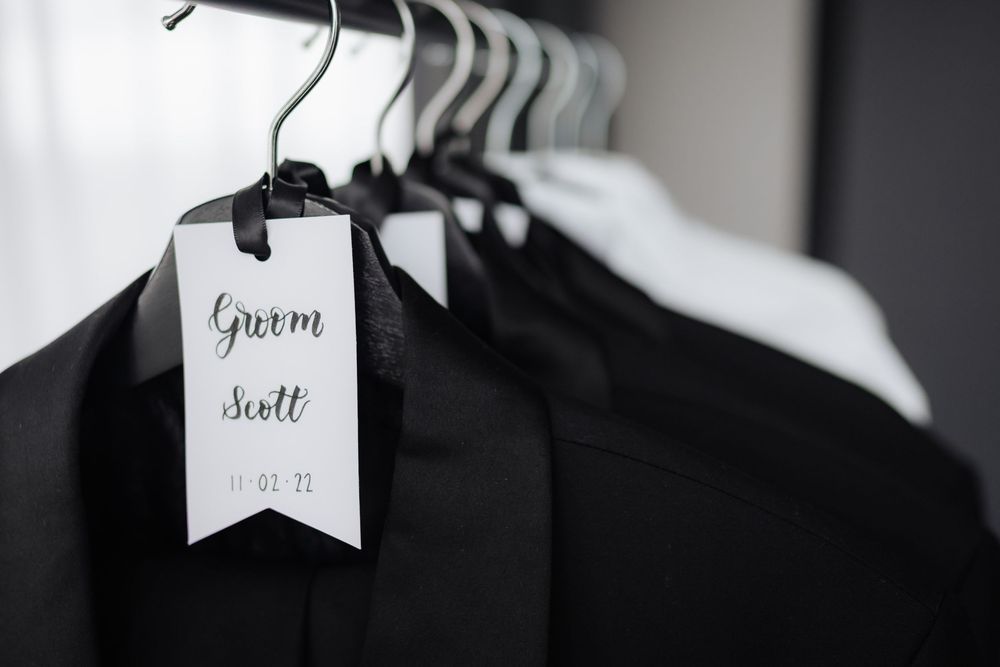 Black suits on hangers with a white tag labeled Groom Scott for a wedding day.