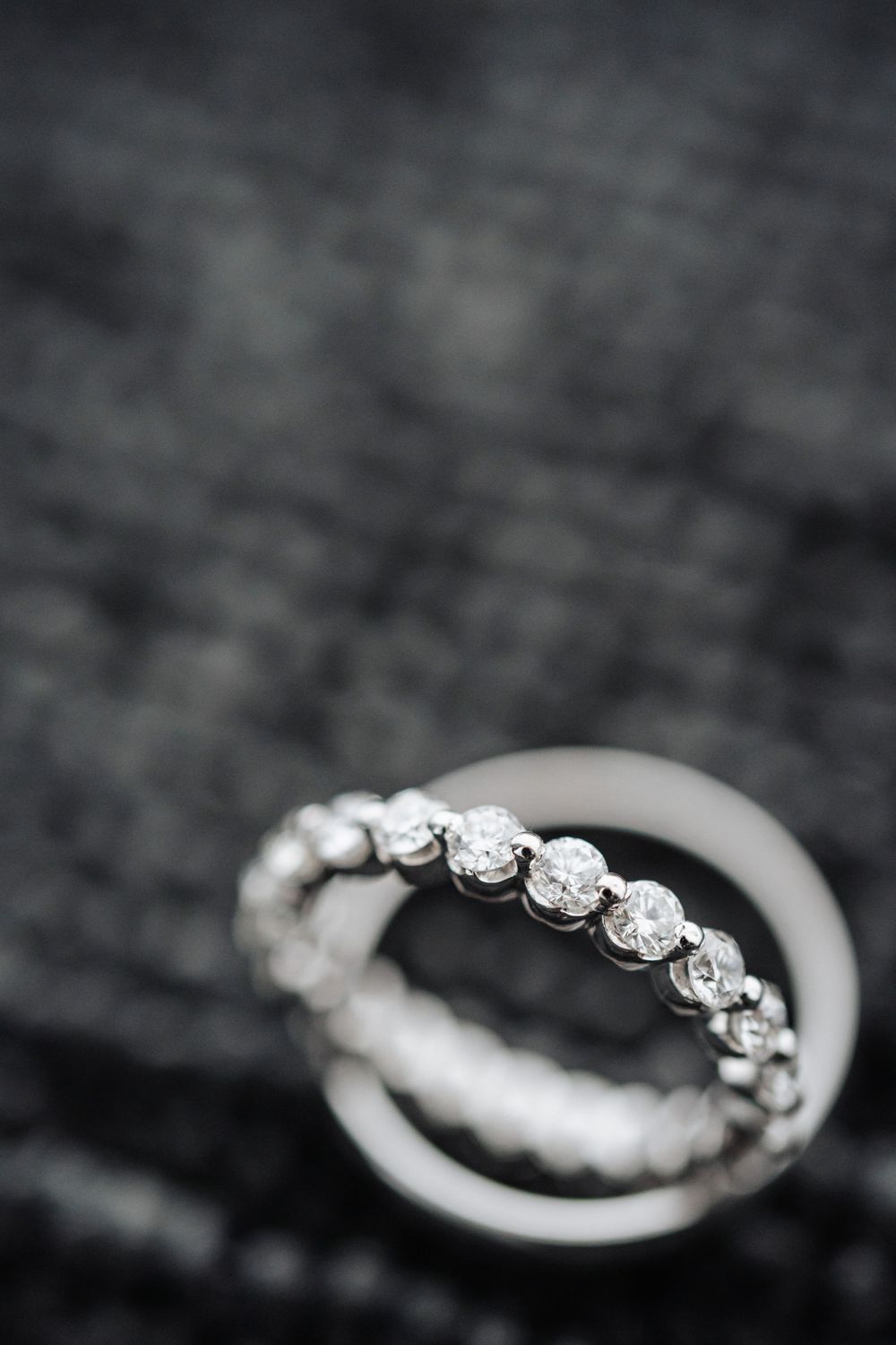Two diamond eternity bands stacked on dark fabric background, showcasing brilliant round-cut stones in white gold setting.