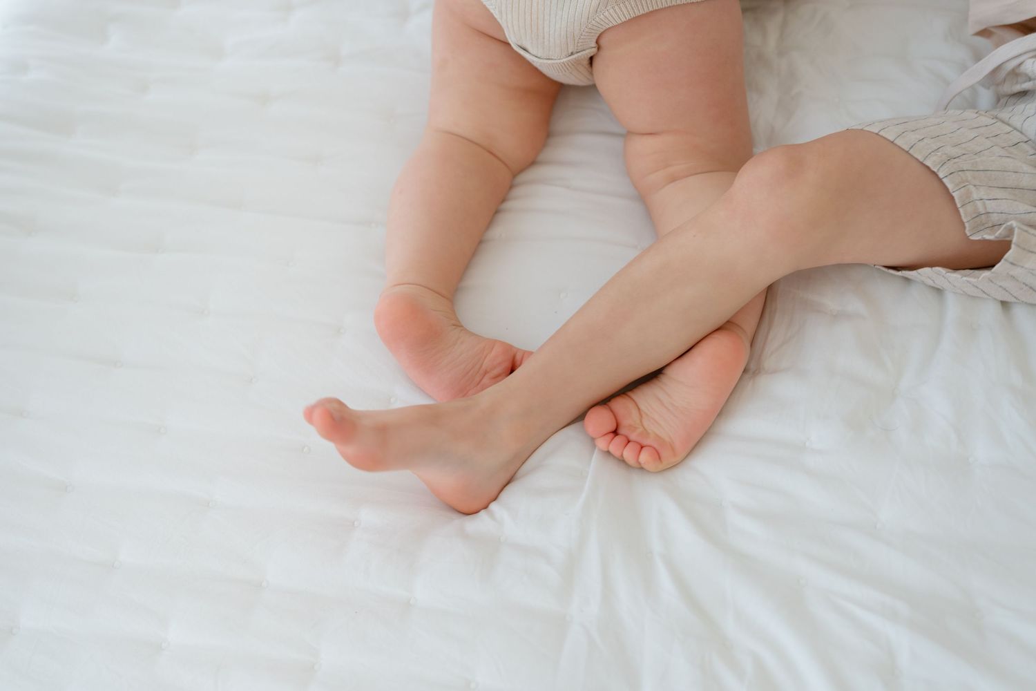 Close-up of baby and adult bare feet resting together on white bedding.