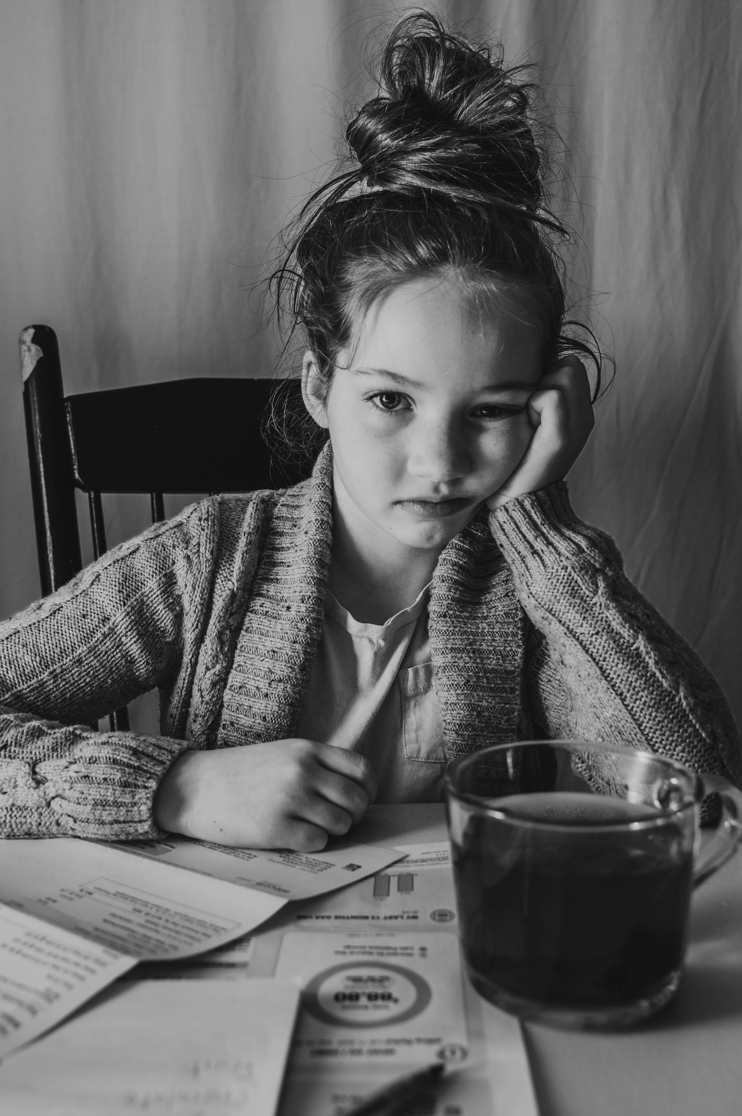 Young girl sitting at a table surrounded by bills and a cup of tea, looking bored, captured by a Brampton lifestyle photographer