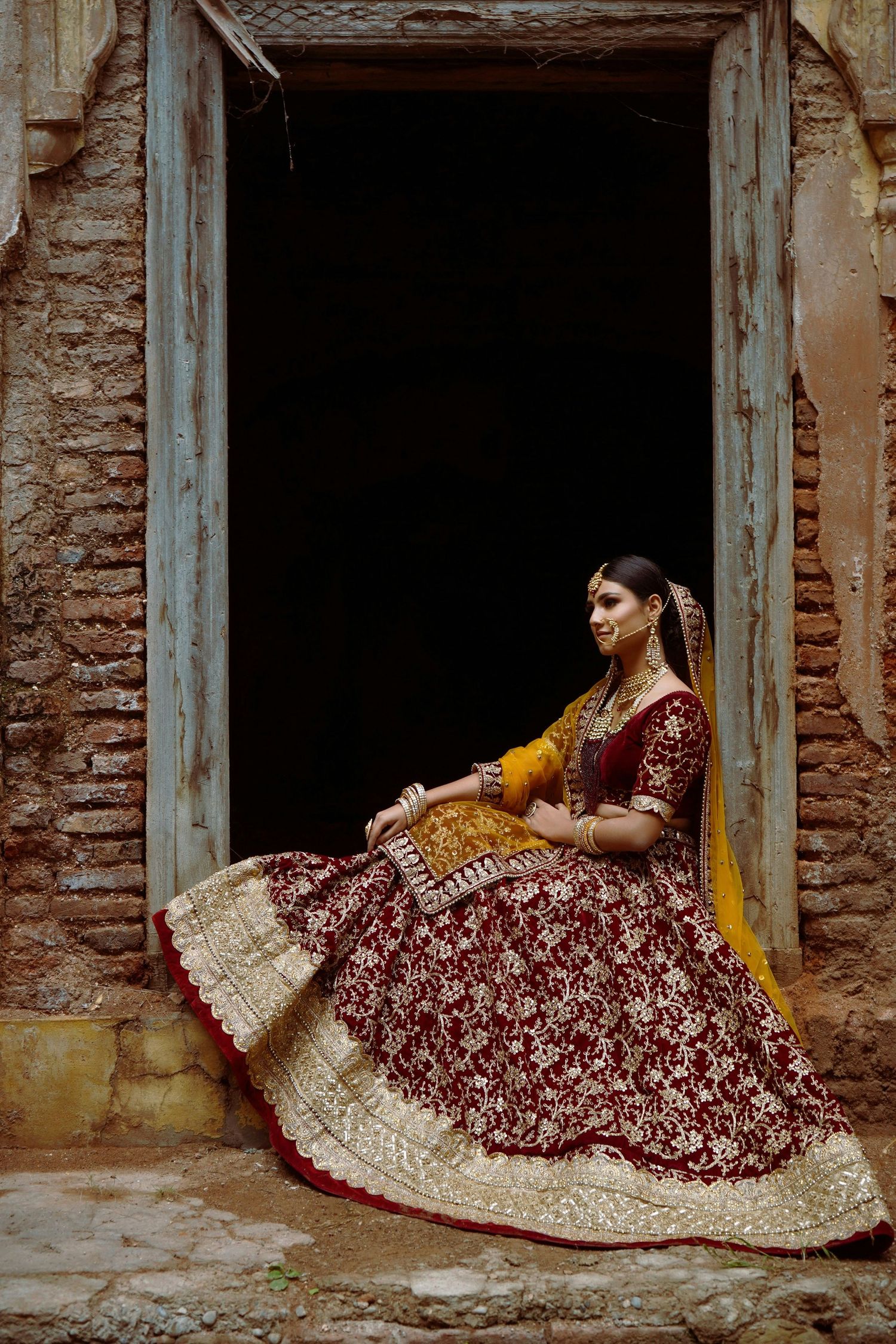 Traditional Indian bridal lehenga in deep maroon and gold embroidery photographed in architectural setting.
