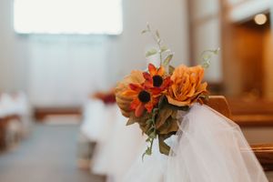 Fall wedding church pew decorated with orange sunflowers, roses, and tulle for an autumn ceremony.