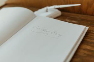 Open wedding guest book titled Our Love Story with a white feather pen on a rustic wooden table.