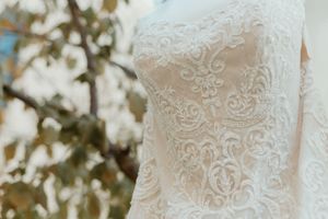 Close-up of elegant white lace wedding dress with intricate floral embroidery detailing, displayed outdoors.