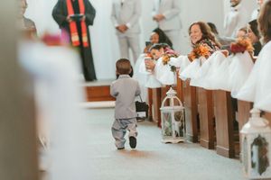 Small child walks down church aisle during wedding ceremony.
