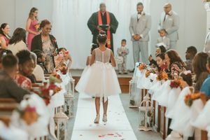 Flower girl walks down white aisle runner in church wedding ceremony.