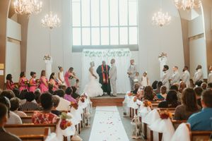 A wedding ceremony in a bright chapel with guests seated in pews as the couple stands at the altar with a officiant.