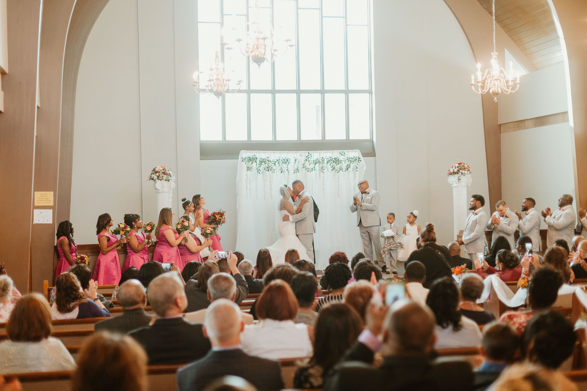 Wedding ceremony at church altar with bridesmaids in pink dresses.