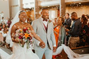 Joyful newlyweds walk down the aisle at their wedding ceremony as guests celebrate with confetti.