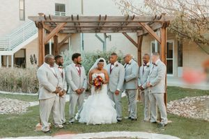 Bride and groomsmen pose outdoors under wooden pergola after wedding.
