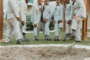 Groomsmen in matching gray suits showing off colorful patterned socks at a wedding ceremony outdoors.