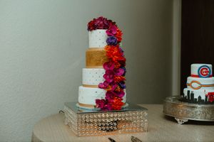 Elegant four-tier white wedding cake adorned with vibrant pink and purple flowers on a crystal stand.