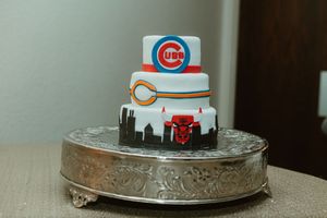 Three-tier Chicago sports themed groom's cake featuring Cubs, Bears, and Bulls logos on a silver stand.