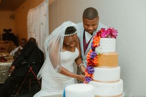 Bride and groom cut colorful floral-decorated four-tier wedding cake.