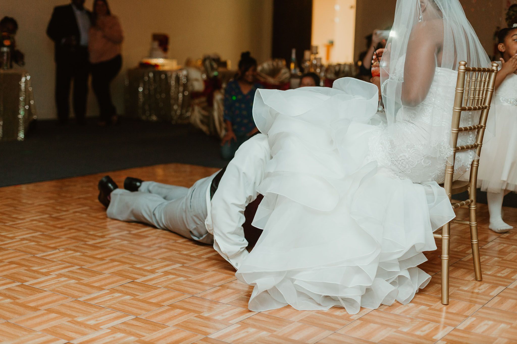 Groom removes garter from bride seated in chair on dance floor at wedding reception.