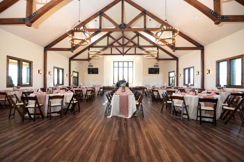 Elegant wedding reception hall with vaulted wooden ceilings, round tables, folding chairs, and blush pink decor.